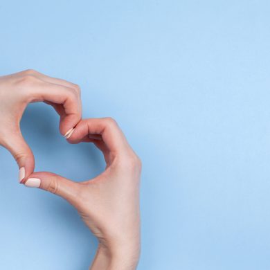 Female hands show a heart symbol on a light blue background. Place for text.