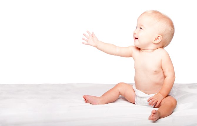 Cute adorable infant baby reaching out with hand asking for something while sitting, on white.